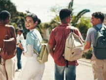 Four students with backpacks walking while engaged in conversation, with one turned around smiling.