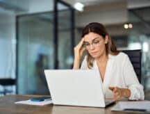 A lady sits at her laptop, frustrated at the newest processing times.
