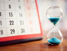 A calendar and an hour glass on a wooden table.