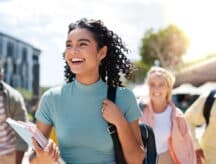 Happy female student with a backpack over one shoulder laughing with her friends.
