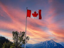 Canada flag flying atop Sulphur Mountain with a sunset view of Banff National Park, and Canadian Rockies in the background.